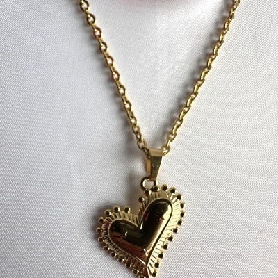 Colar dourado com pendente em forma de coração sobre tecido branco