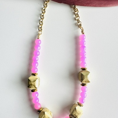 Colar com contas rosa e douradas sobre fundo branco e tecido vermelho.