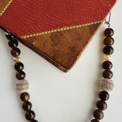 Colar com contas castanhas e cristais sobre couro vermelho e castanho