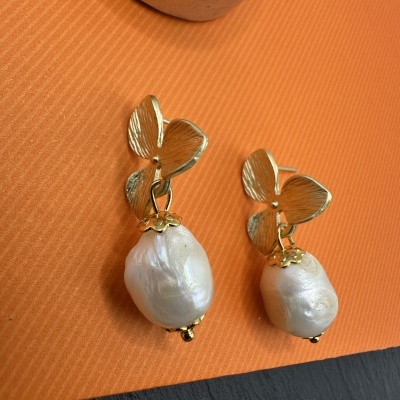 Brincos dourados com folhas e pérolas barrocas sobre fundo laranja