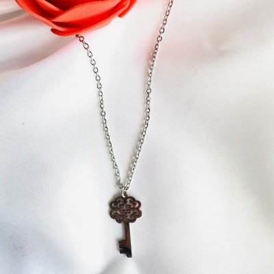 Colar com pendente chave metálica prateada e rosa vermelha sobre tecido branco