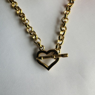 Colar dourado com corrente e fecho em forma de coração sobre tecido branco