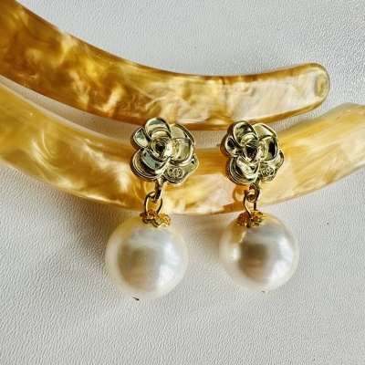 Brincos dourados com pérolas penduradas sobre presilhas bege marmoreadas