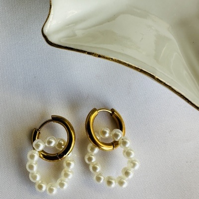 Brincos dourados com pérolas em tecido branco perto de cerâmica