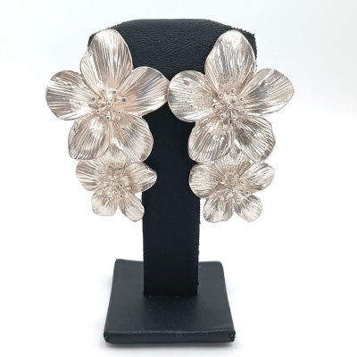 Brincos em metal prateado com flores expostos em suporte preto.