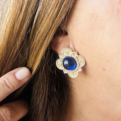 Brinco dourado em forma de flor com pedra azul na orelha