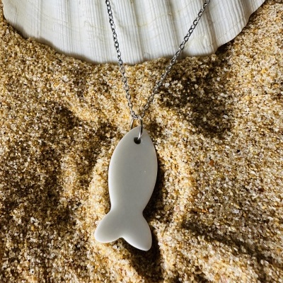 Colar com pendente de peixe branco na areia junto a uma concha