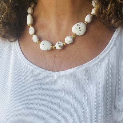 Colar com contas brancas manchadas castanhas e contas douradas numa pessoa com blusa branca