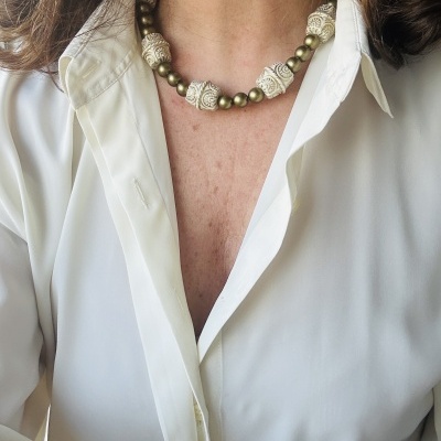 Colar artesanal com contas grandes e pequenas em tons de branco e dourado em cima de camisa branca