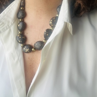 Colar preto com manchas douradas e pequenas esferas douradas usado sobre camisa branca