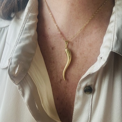 Colar dourado com pendente em forma de corno numa pessoa com camisa branca
