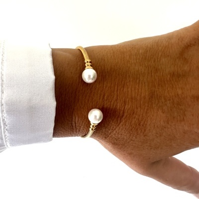 Pulseira dourada com pérolas brancas num pulso de pele castanha e camisa branca