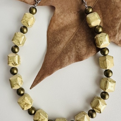 Colar com contas douradas e verdes sobre folha seca castanha