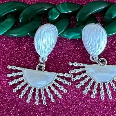 Brincos prateados com design de gota e franja sobre superfície rosa brilhante e corrente verde