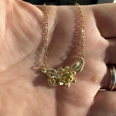 Colar dourado com flores e folhas segurado na mão