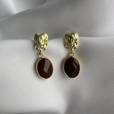 Brincos dourados com pedra castanha facetada sobre tecido branco.