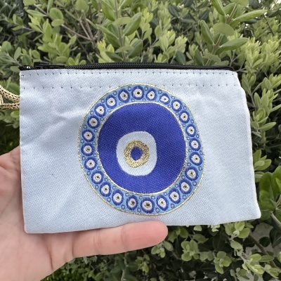 Carteira de tecido cinza claro com bordado circular azul e dourado, segurada à mão