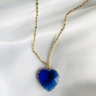 Colar dourado com pendente azul coração sobre tecido branco.