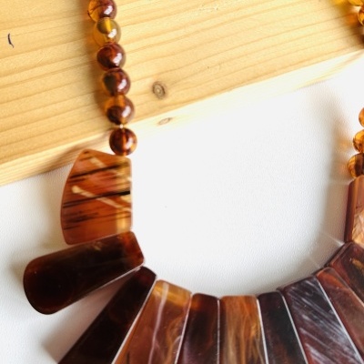 Colar castanho em contas redondas pequenas e pendentes trapezoidais e semicirculares sobre madeira clara
