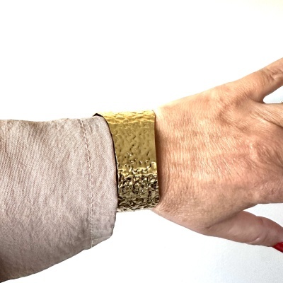 Braçadeira dourada texturizada no pulso de uma mão