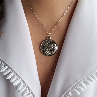 Colar com pendente de sol metálico prateado numa camisa branca com renda