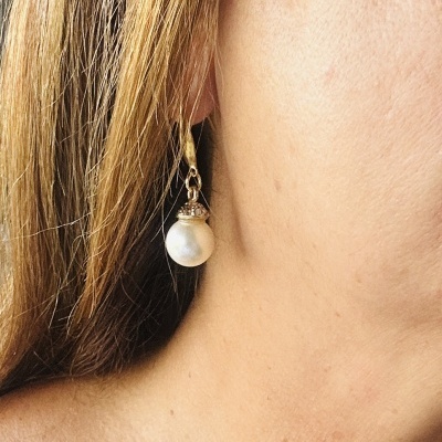Brinco pendente com pérola branca redonda e detalhe dourado numa orelha feminina