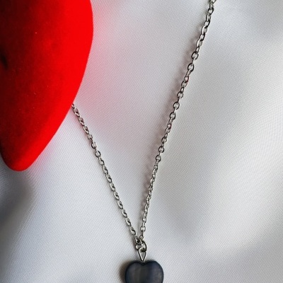 Colar com pendente de coração preto sobre fundo branco e objeto vermelho ao lado