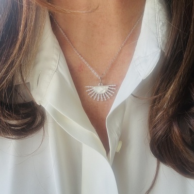 Colar prateado com pendente em leque em pescoço sobre camisa branca