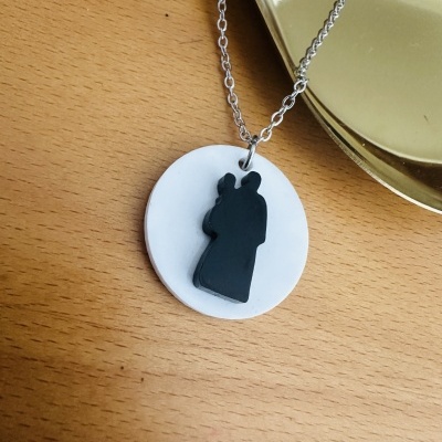 Colar com pendente redondo branco e silhueta preta de duas figuras abraçadas