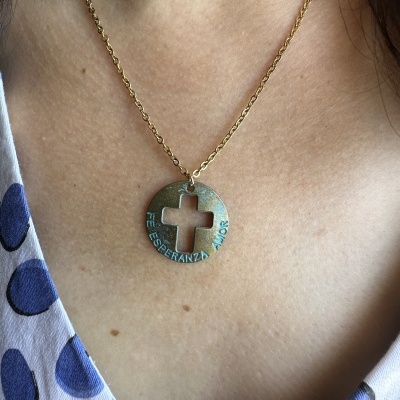 Colar dourado com pendente redondo e recorte de cruz com texto gravado usado no pescoço