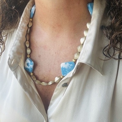 Colar com contas bege e azuis usado sobre camisa bege clara