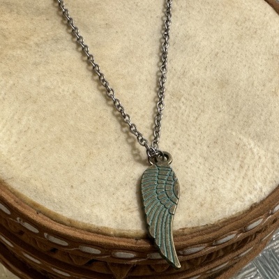 Colar com pendente de asa azul esverdeada sobre tambor de madeira e pele clara.