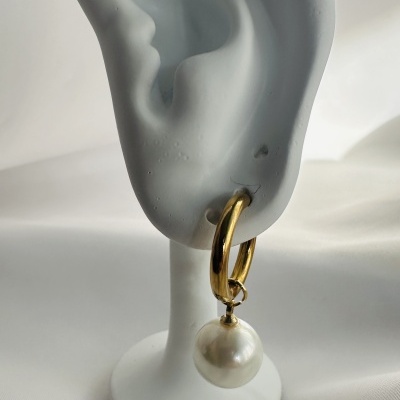 Brinco dourado com pérola exibido em suporte branco em forma de orelha