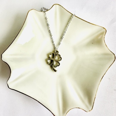 Colar com trevo de quatro folhas numa tigela branca com bordas douradas