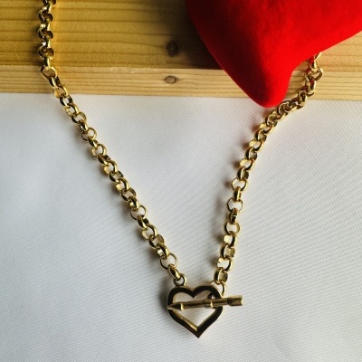 Colar dourado com fecho coração sobre tecido branco