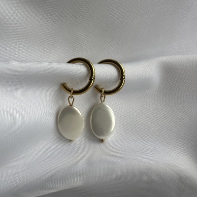 Brincos dourados com pendente oval branco em tecido branco.