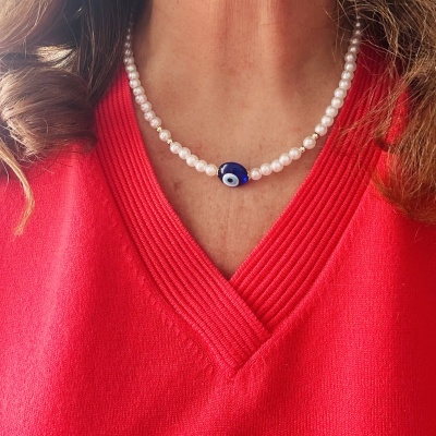 Colar de pérolas brancas com pendente de olho azul escuro em camisola vermelha.