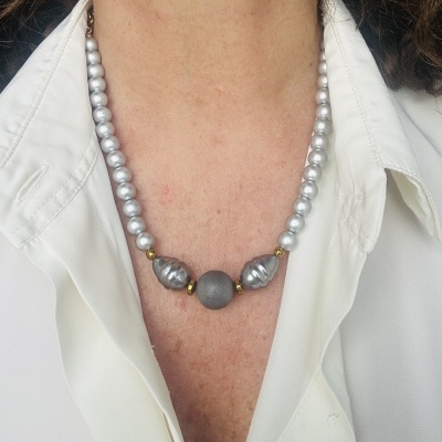 Colar com pérolas prateadas e contas douradas usado sobre camisa branca