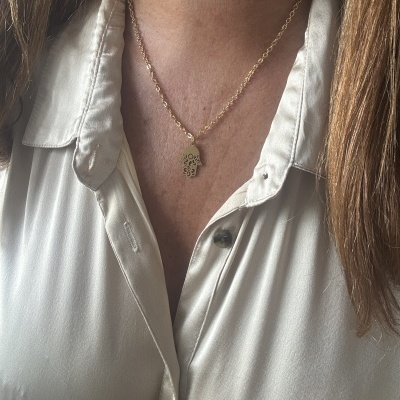 Colar dourado com pendente em forma de mão usado com camisa bege.