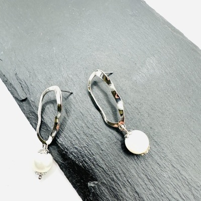 Brincos prateados com pendente branco sobre placa de ardósia preta