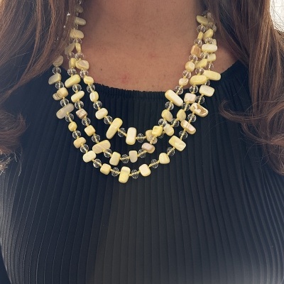 Colar feminino de várias voltas com contas amarelas, creme e transparentes, em blusa preta plissada.