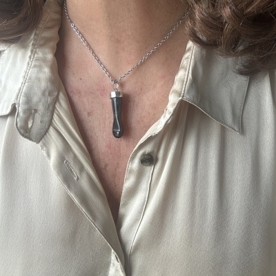 Colar com pendente preto e prata, corrente prateada, em pessoa com camisa bege clara