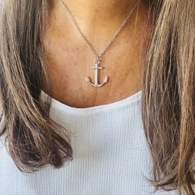 Colar prateado com pendente de âncora em pessoa com camisa branca