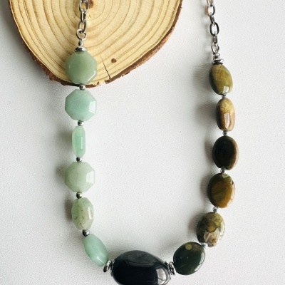 Colar de pedras naturais em tons verdes e castanhos com corrente metálica sobre fundo branco e madeira