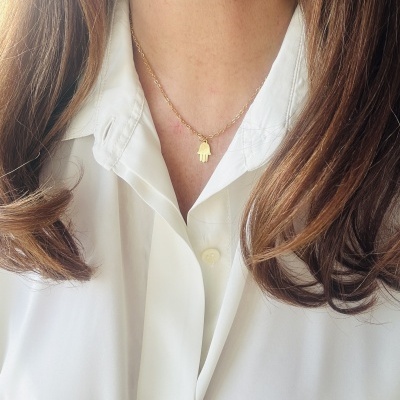 Colar dourado com pendente em forma de mão, pessoa com camisa branca