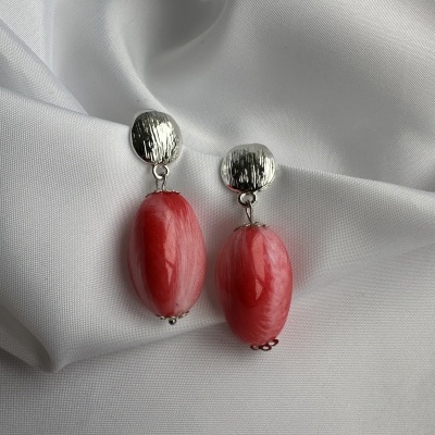 Brincos com base prateada e pendente vermelho em resina sobre tecido branco