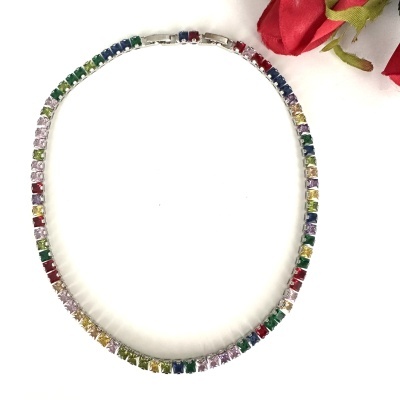 Colar com pedras coloridas em fundo branco e flores vermelhas ao lado