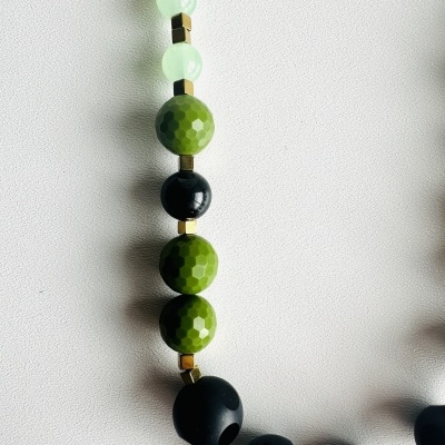 Colar com contas pretas, verdes e cubos dourados em fundo branco