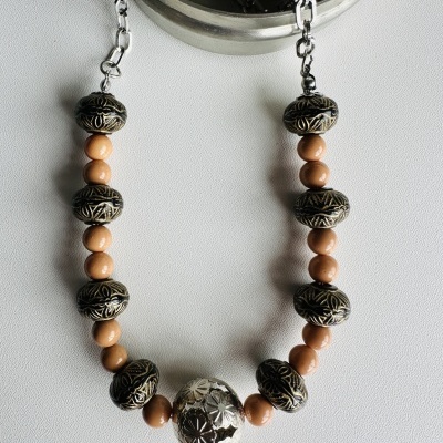 Colar com contas metálicas e madeira sobre superfície branca