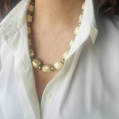 Colar de contas grandes irregulares bege e marrons numa camisa branca.